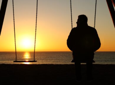 How I Met My Big Brother 2 A person sits alone on a swing facing the ocean during sunset. The sun is low on the horizon, casting a warm glow over the water. Another swing, like a silent echo of their thoughts, is empty next to them. The scene has a serene and contemplative atmosphere, reminiscent of moments in "how i met my big brother.